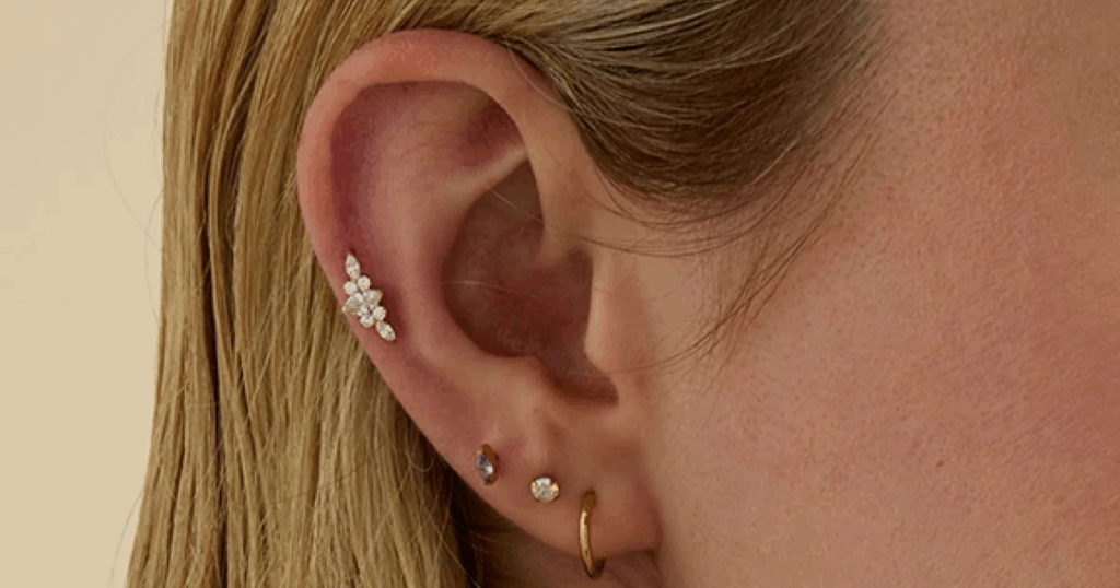 
A close-up of a person's ear shows a series of earrings, including an ornate piece, featuring hypoallergenic jewelry for travel from Wulf Diamond Jewelers.